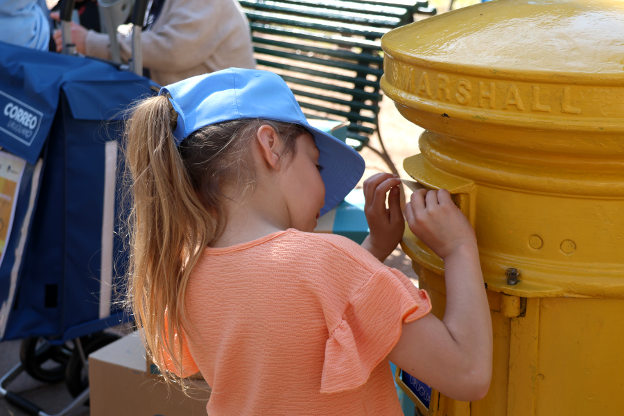 Una niña deposita su postal en el antiguo buzón