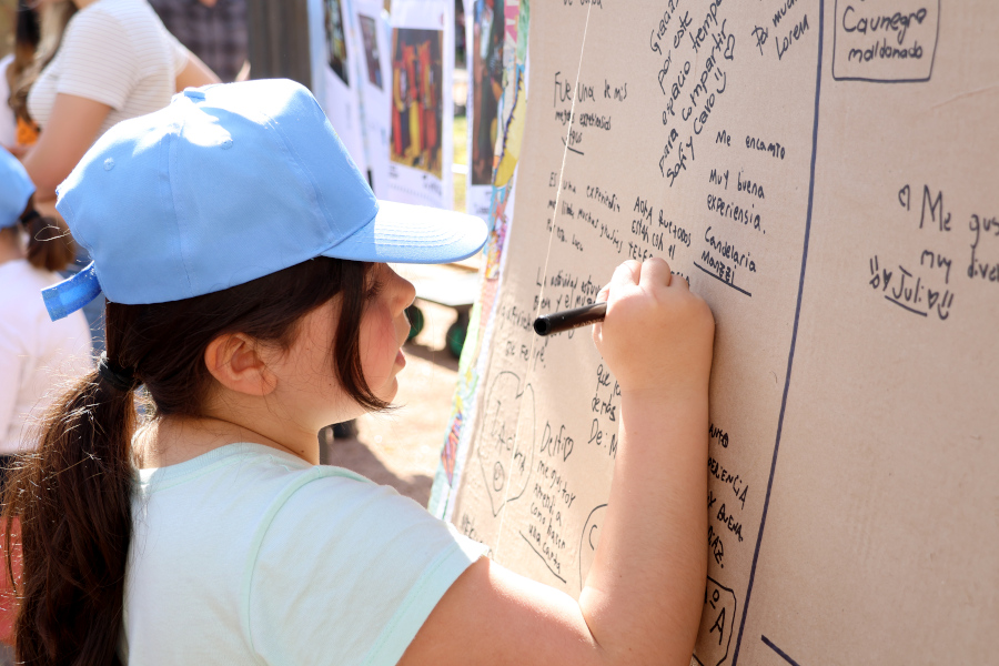 Una niña escribe su dedicatoria en una gran postal colocada en el espacio del taller